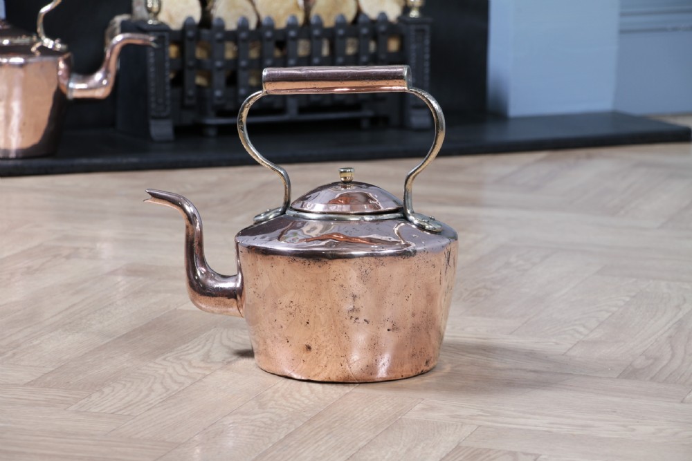 An antique George III polished copper kettle featuring a brass finial lid, overhead handle, and curved spout. View II