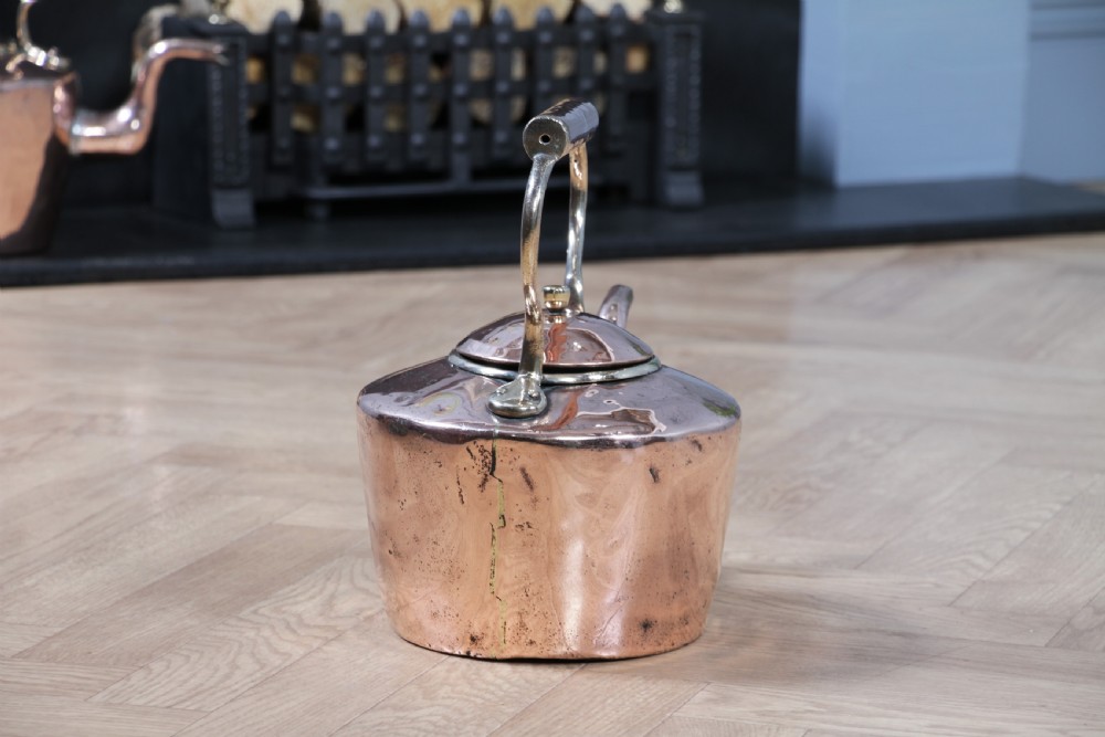 An antique George III polished copper kettle featuring a brass finial lid, overhead handle, and curved spout. View III