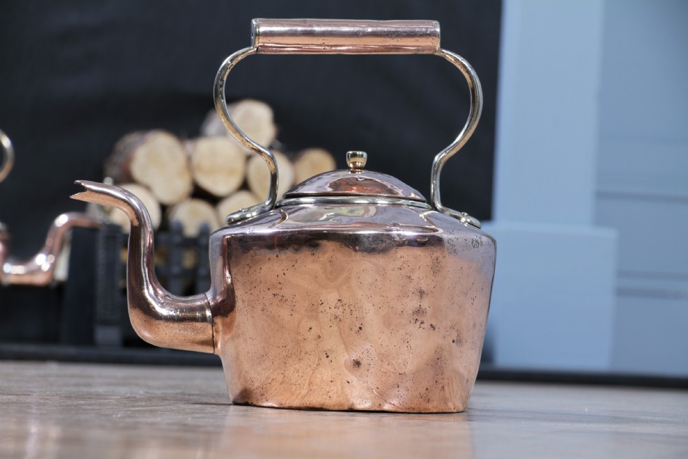 An antique George III polished copper kettle featuring a brass finial lid, overhead handle, and curved spout. View VI