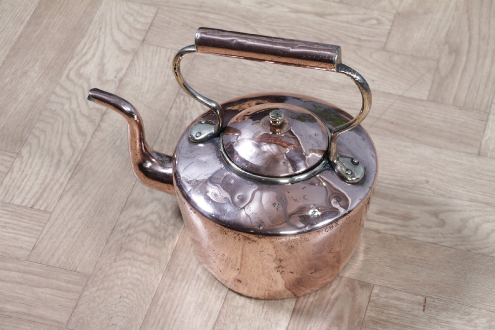 An antique George III polished copper kettle featuring a brass finial lid, overhead handle, and curved spout. View VIII