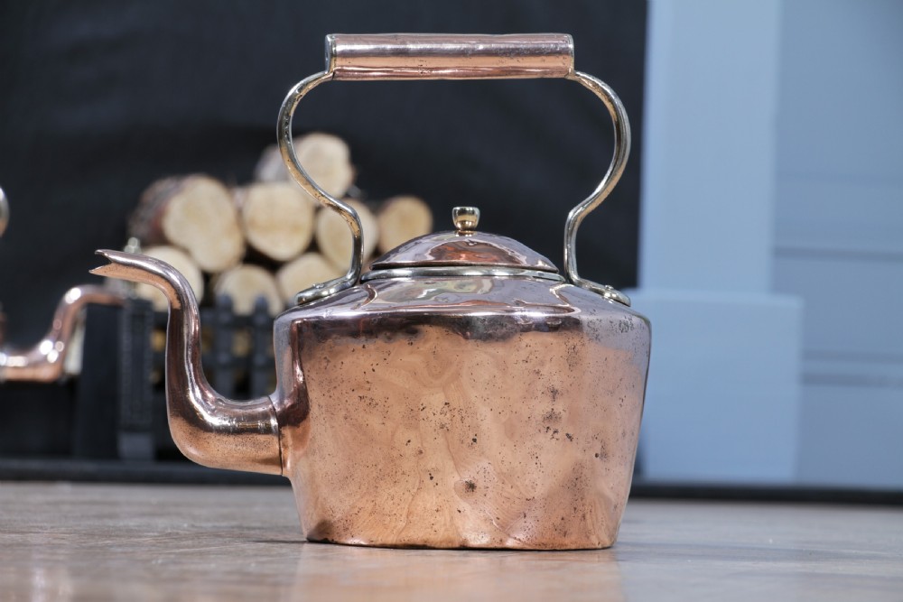 An antique George III polished copper kettle featuring a brass finial lid, overhead handle, and curved spout. View XII