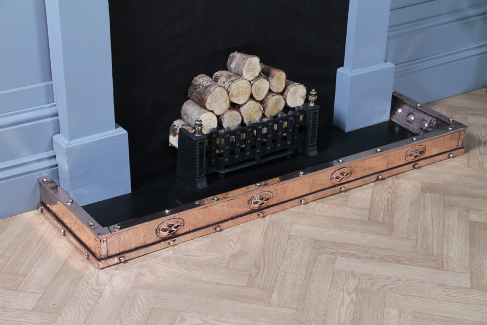 A low polished copper fireplace fender curb featuring hand-riveted edges and decorative embossed oval motifs around the perimeter. View II