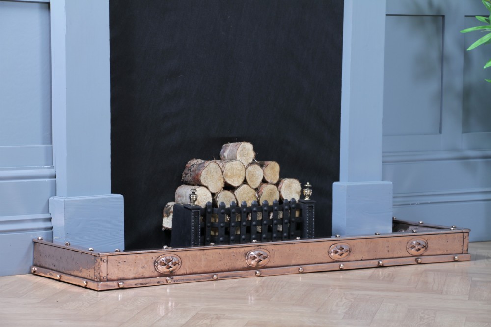 A low polished copper fireplace fender curb featuring hand-riveted edges and decorative embossed oval motifs around the perimeter. View III
