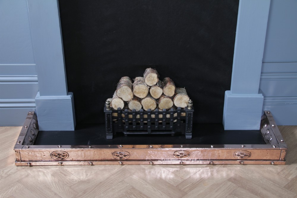 A low polished copper fireplace fender curb featuring hand-riveted edges and decorative embossed oval motifs around the perimeter. View IV