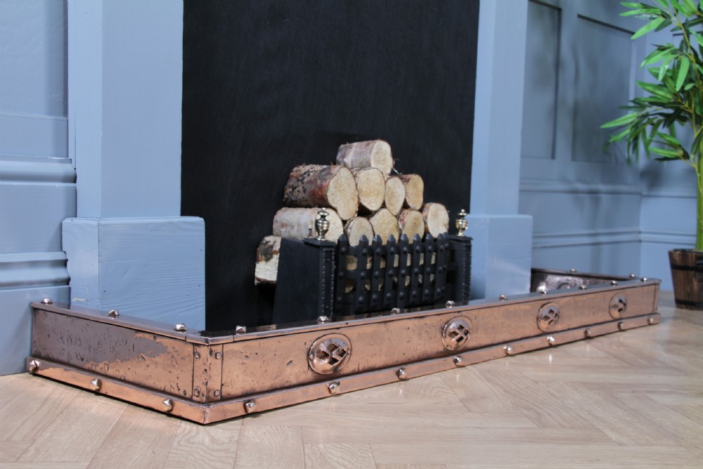 A low polished copper fireplace fender curb featuring hand-riveted edges and decorative embossed oval motifs around the perimeter. View V