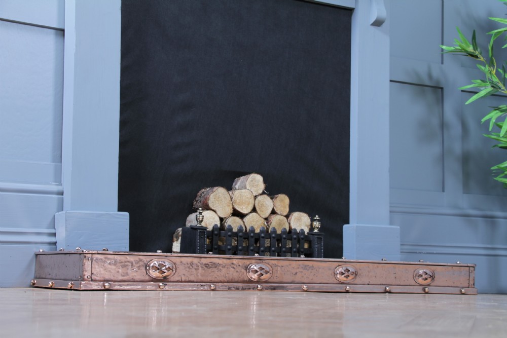 A low polished copper fireplace fender curb featuring hand-riveted edges and decorative embossed oval motifs around the perimeter. View VII