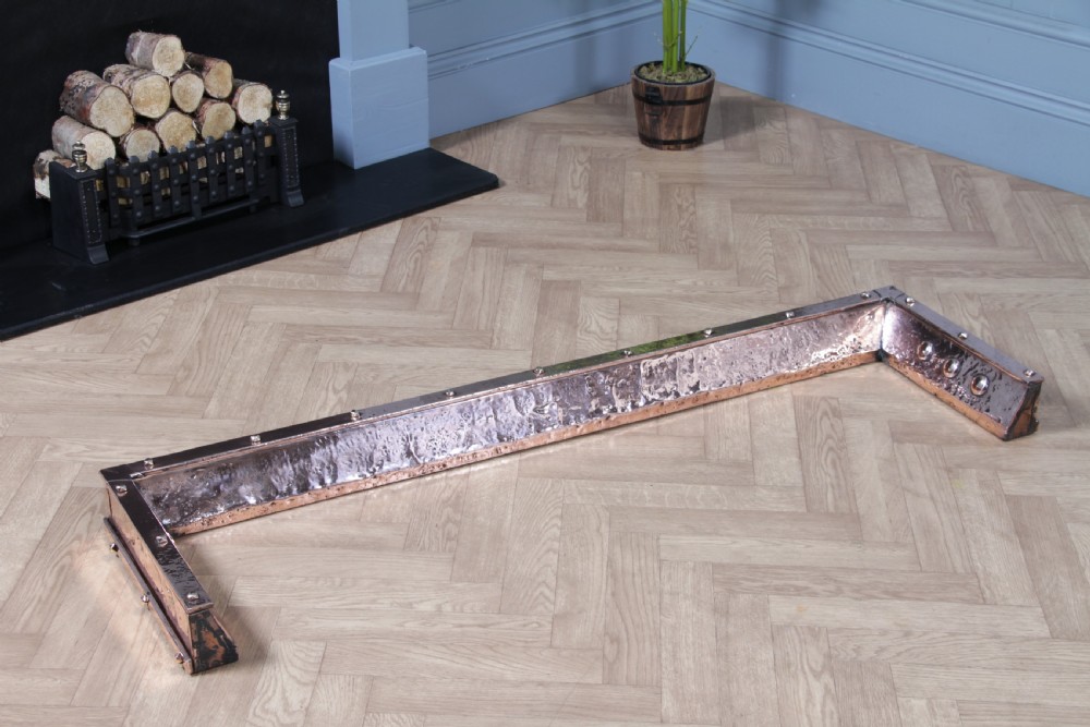 A low polished copper fireplace fender curb featuring hand-riveted edges and decorative embossed oval motifs around the perimeter. View VIII