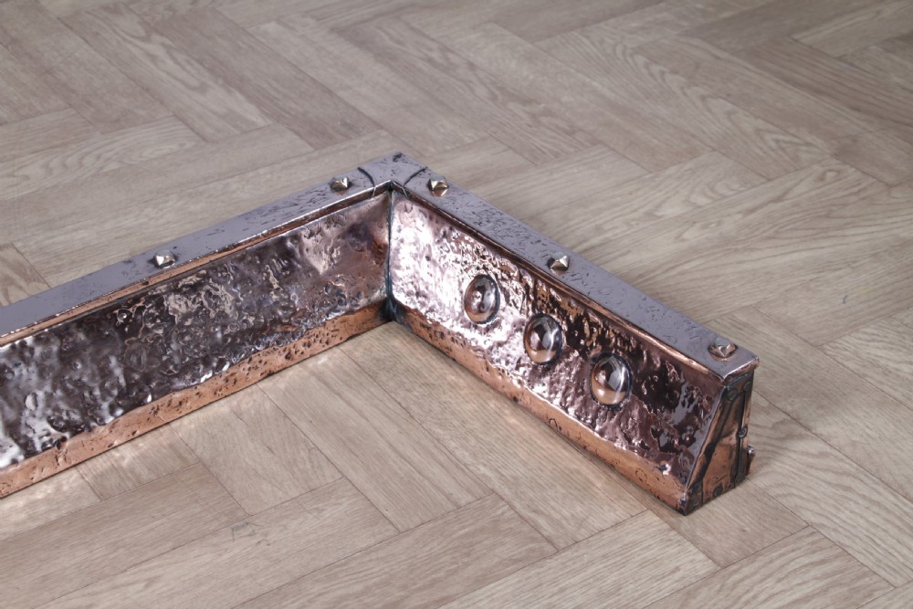 A low polished copper fireplace fender curb featuring hand-riveted edges and decorative embossed oval motifs around the perimeter. View IX