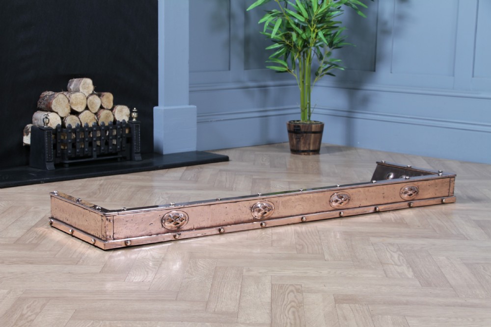 A low polished copper fireplace fender curb featuring hand-riveted edges and decorative embossed oval motifs around the perimeter. View X