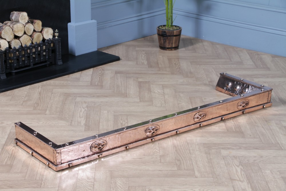 A low polished copper fireplace fender curb featuring hand-riveted edges and decorative embossed oval motifs around the perimeter. View XI