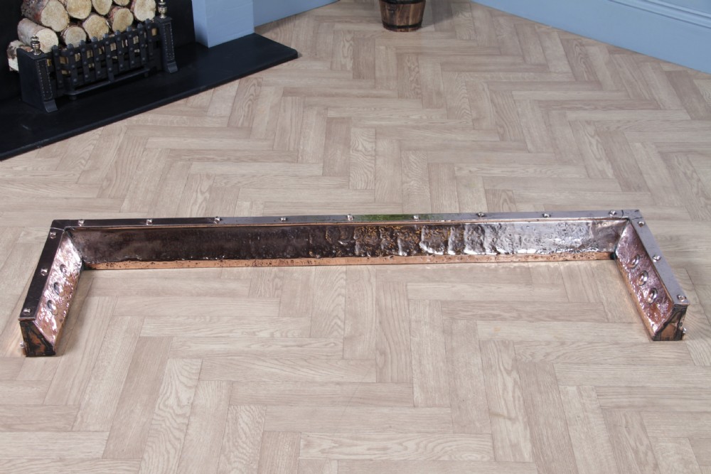 A low polished copper fireplace fender curb featuring hand-riveted edges and decorative embossed oval motifs around the perimeter. View XII