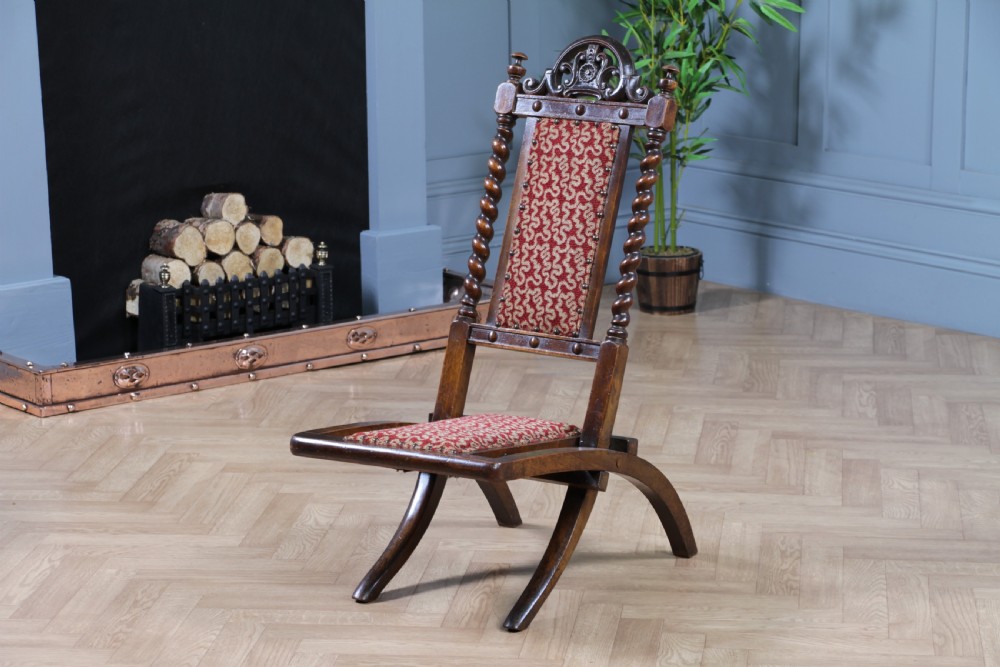 Late Victorian dark wood folding chair featuring barley twist uprights, a carved crest rail, red patterned upholstery, and brass stud trim.