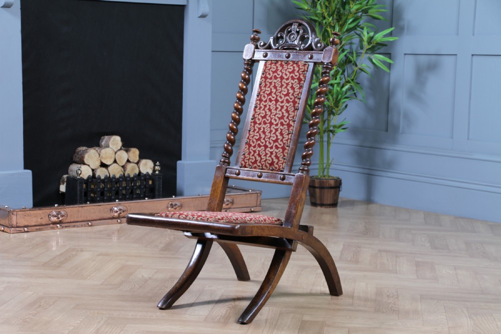 Late Victorian dark wood folding chair featuring barley twist uprights, a carved crest rail, red patterned upholstery, and brass stud trim. View II