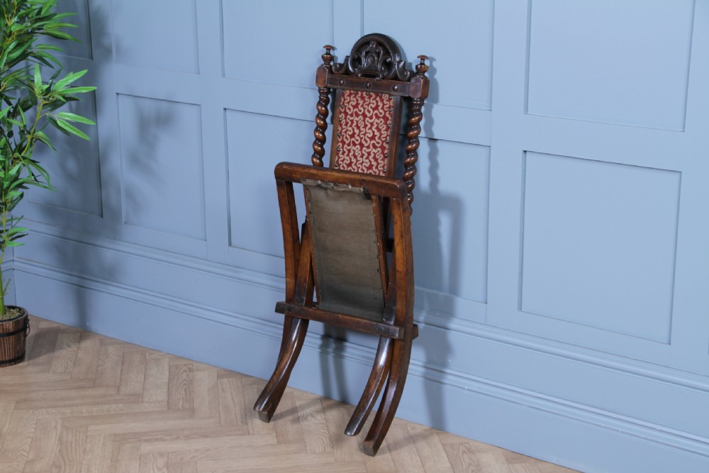 Late Victorian dark wood folding chair featuring barley twist uprights, a carved crest rail, red patterned upholstery, and brass stud trim. View V