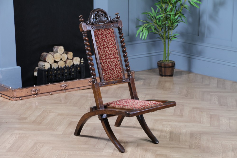 Late Victorian dark wood folding chair featuring barley twist uprights, a carved crest rail, red patterned upholstery, and brass stud trim. View VI