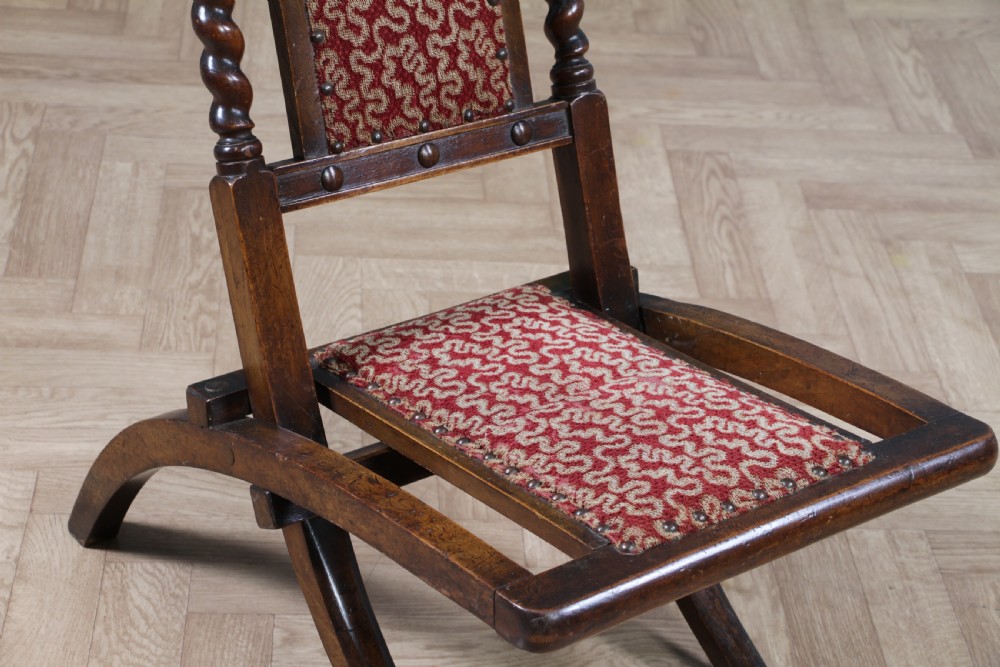 Late Victorian dark wood folding chair featuring barley twist uprights, a carved crest rail, red patterned upholstery, and brass stud trim. View VII