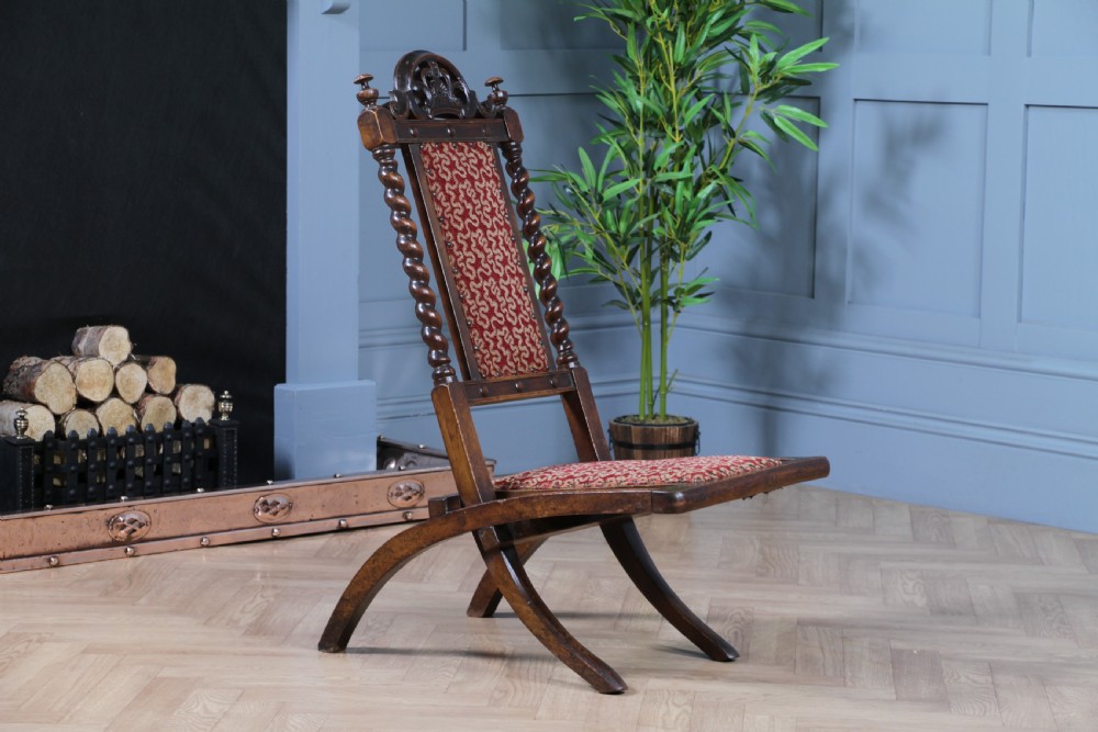 Late Victorian dark wood folding chair featuring barley twist uprights, a carved crest rail, red patterned upholstery, and brass stud trim. View IX