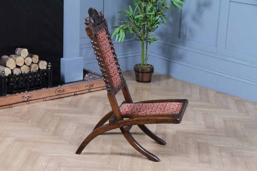 Late Victorian dark wood folding chair featuring barley twist uprights, a carved crest rail, red patterned upholstery, and brass stud trim. View X