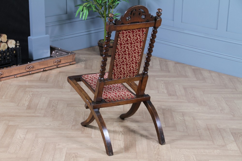 Late Victorian dark wood folding chair featuring barley twist uprights, a carved crest rail, red patterned upholstery, and brass stud trim. View XI