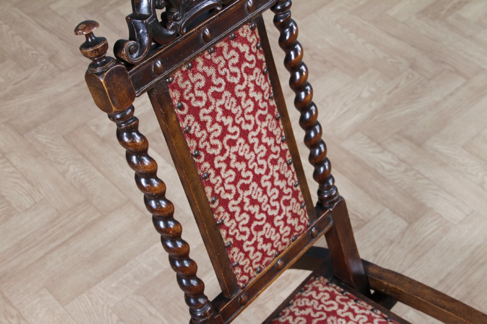 Late Victorian dark wood folding chair featuring barley twist uprights, a carved crest rail, red patterned upholstery, and brass stud trim. View XIV