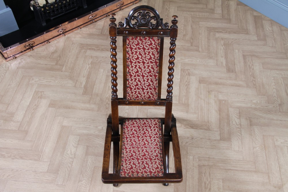 Late Victorian dark wood folding chair featuring barley twist uprights, a carved crest rail, red patterned upholstery, and brass stud trim. View XV