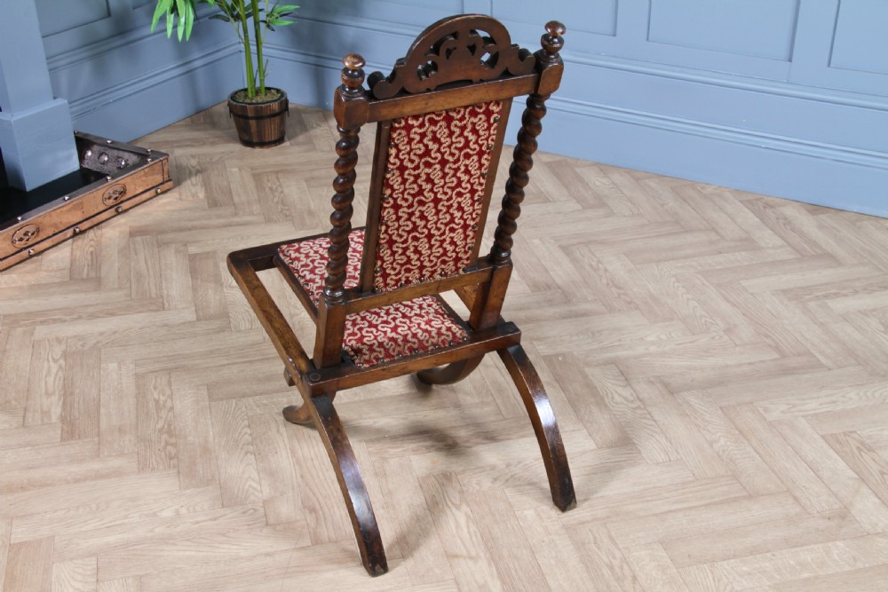 Late Victorian dark wood folding chair featuring barley twist uprights, a carved crest rail, red patterned upholstery, and brass stud trim. View XVII