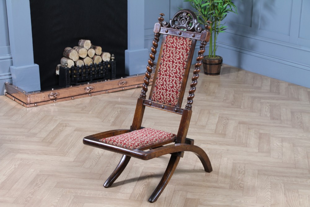 Late Victorian dark wood folding chair featuring barley twist uprights, a carved crest rail, red patterned upholstery, and brass stud trim. View XVIII
