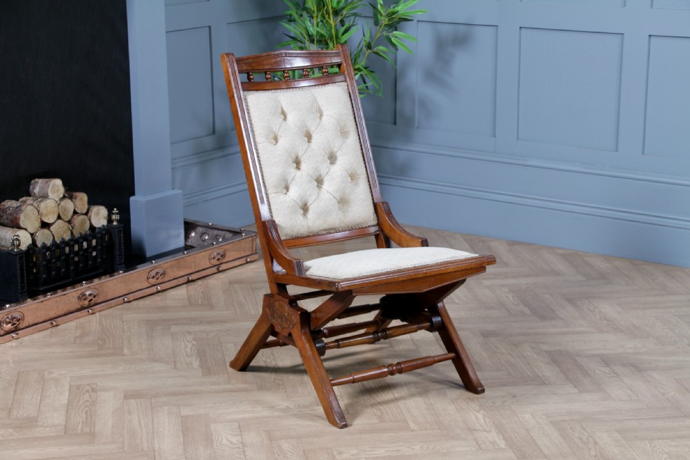 An Edwardian walnut platform rocking chair featuring cream button-backed upholstery and turned wooden spindles on a stationary crossed base.
