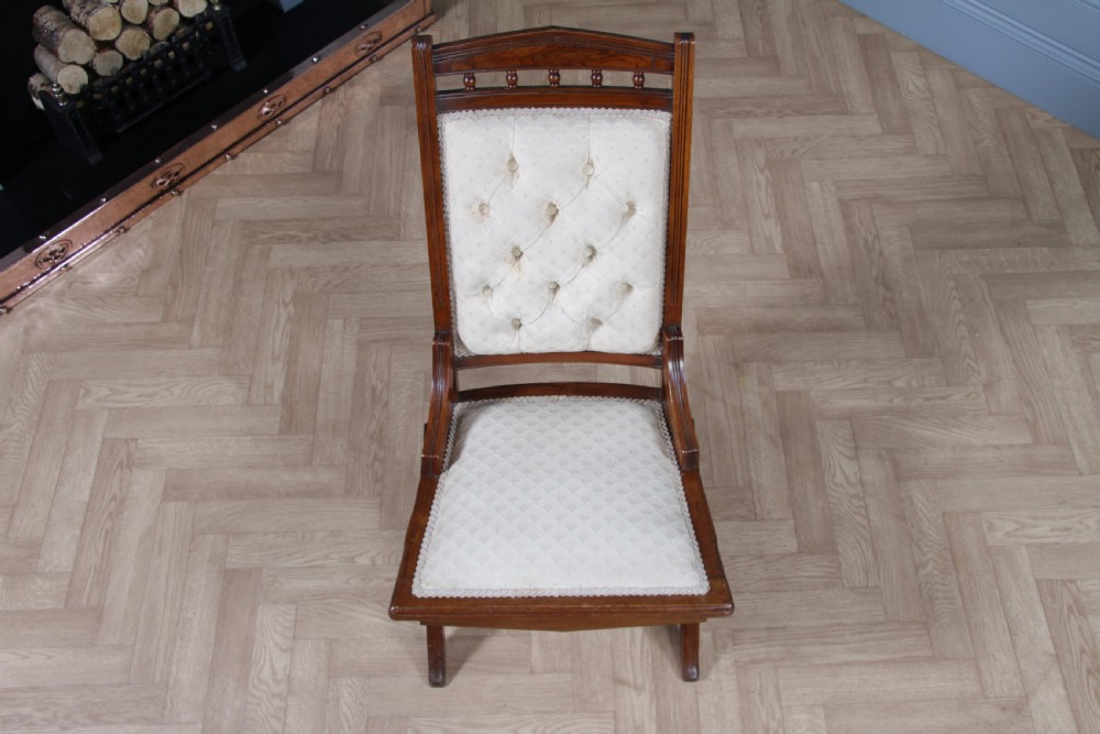 An Edwardian walnut platform rocking chair featuring cream button-backed upholstery and turned wooden spindles on a stationary crossed base. View IX