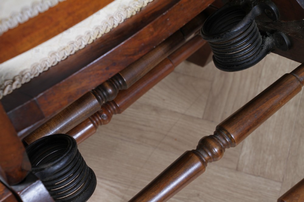 An Edwardian walnut platform rocking chair featuring cream button-backed upholstery and turned wooden spindles on a stationary crossed base. View XII
