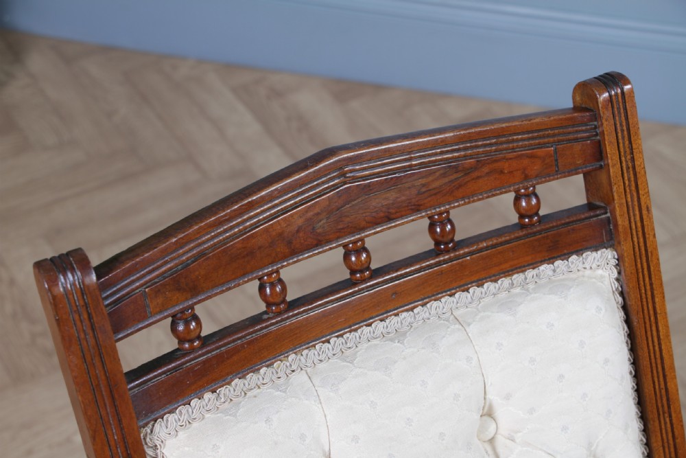 An Edwardian walnut platform rocking chair featuring cream button-backed upholstery and turned wooden spindles on a stationary crossed base. View XIII