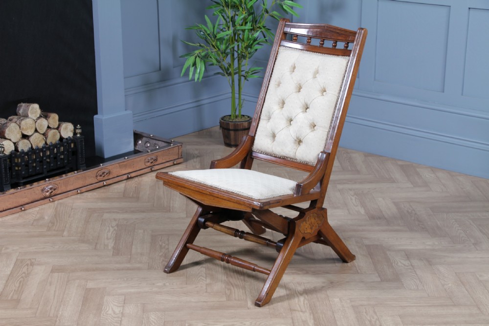 An Edwardian walnut platform rocking chair featuring cream button-backed upholstery and turned wooden spindles on a stationary crossed base. View XVI