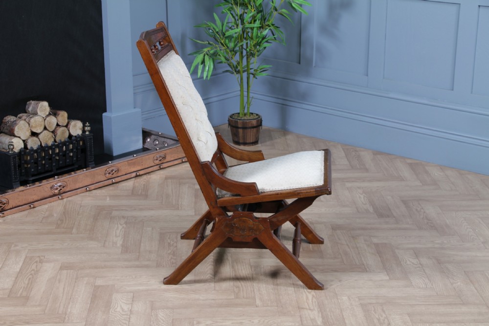 An Edwardian walnut platform rocking chair featuring cream button-backed upholstery and turned wooden spindles on a stationary crossed base. View XIX