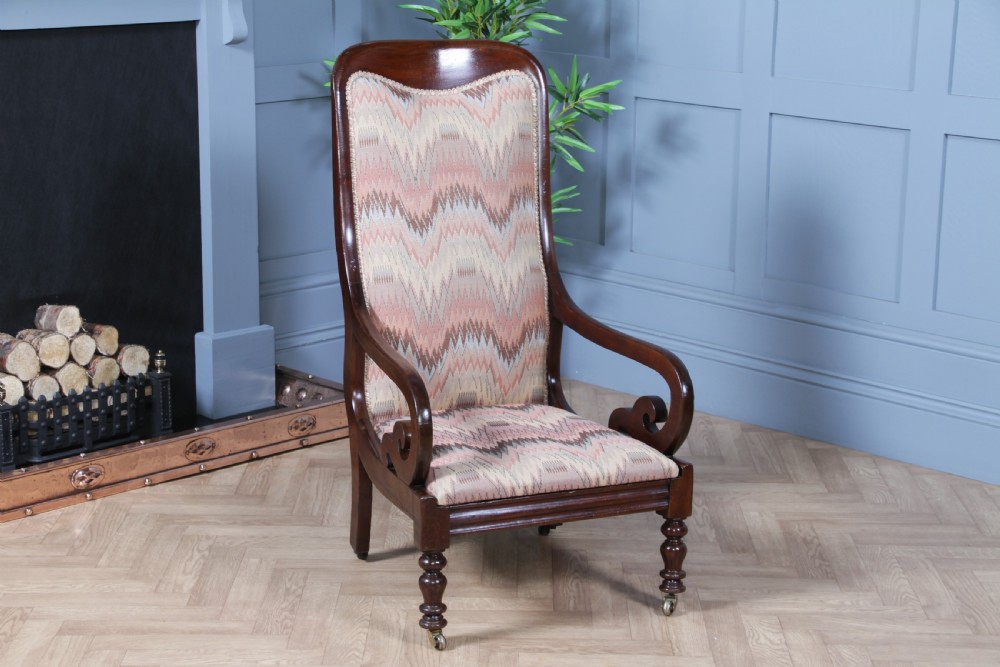 A high-backed Victorian mahogany fireside armchair featuring geometric flame-patterned upholstery, curved scroll armrests, turned front legs on brass castors, and a dark polished finish.