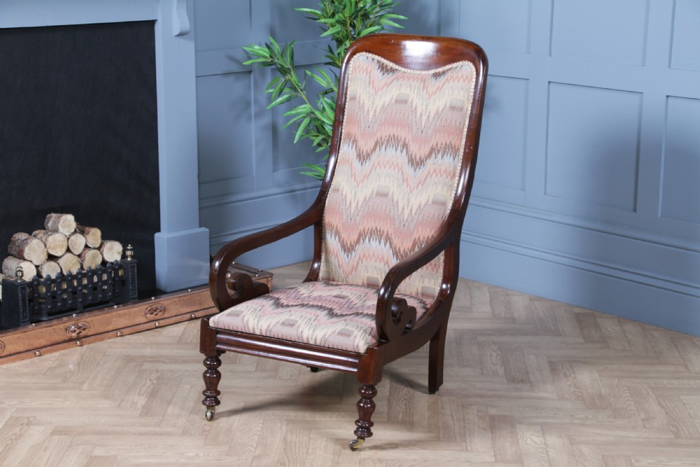 A high-backed Victorian mahogany fireside armchair featuring geometric flame-patterned upholstery, curved scroll armrests, turned front legs on brass castors, and a dark polished finish. View II