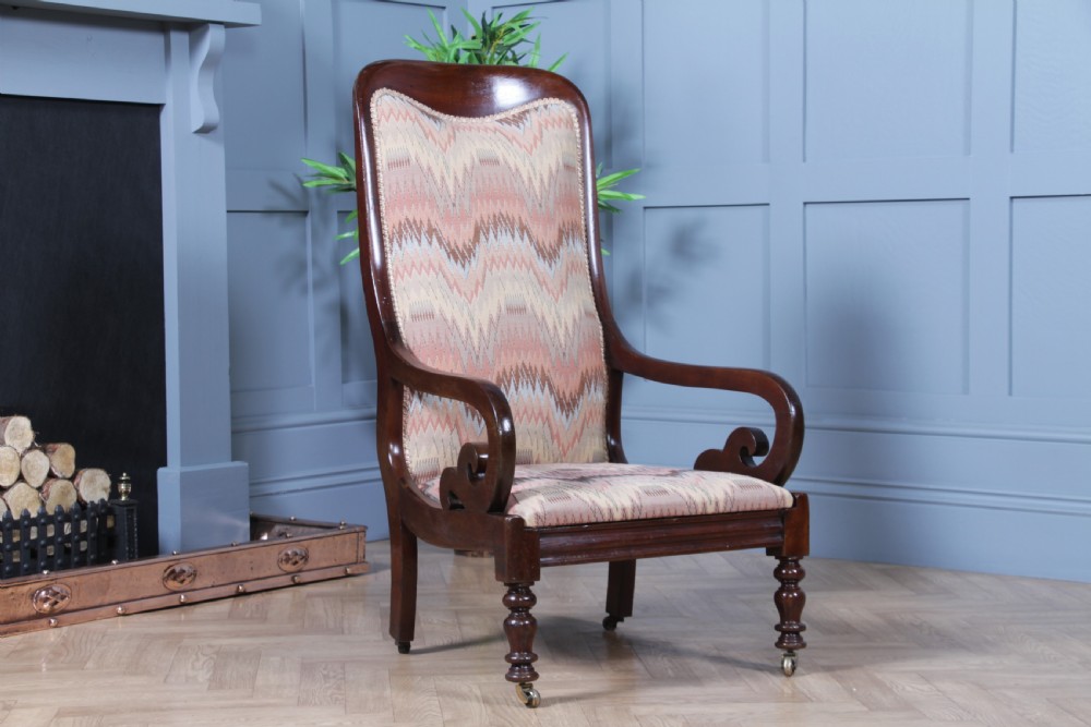 A high-backed Victorian mahogany fireside armchair featuring geometric flame-patterned upholstery, curved scroll armrests, turned front legs on brass castors, and a dark polished finish. View III