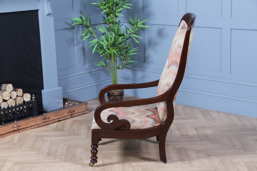 A high-backed Victorian mahogany fireside armchair featuring geometric flame-patterned upholstery, curved scroll armrests, turned front legs on brass castors, and a dark polished finish. View IV