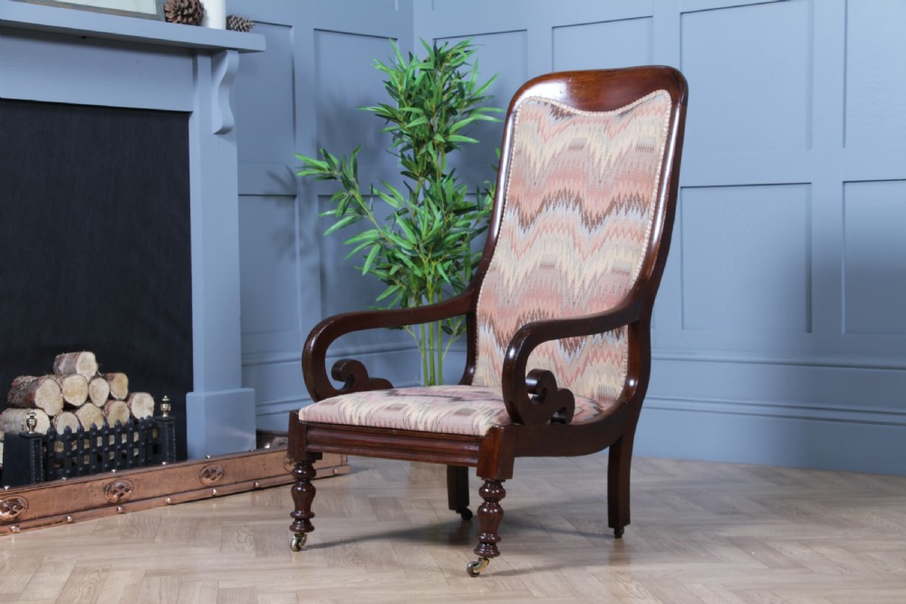 A high-backed Victorian mahogany fireside armchair featuring geometric flame-patterned upholstery, curved scroll armrests, turned front legs on brass castors, and a dark polished finish. View V