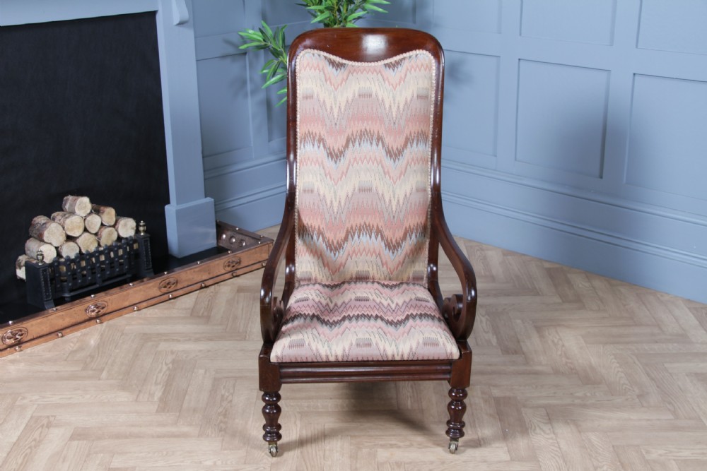 A high-backed Victorian mahogany fireside armchair featuring geometric flame-patterned upholstery, curved scroll armrests, turned front legs on brass castors, and a dark polished finish. View VII