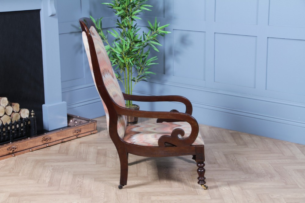 A high-backed Victorian mahogany fireside armchair featuring geometric flame-patterned upholstery, curved scroll armrests, turned front legs on brass castors, and a dark polished finish. View VIII