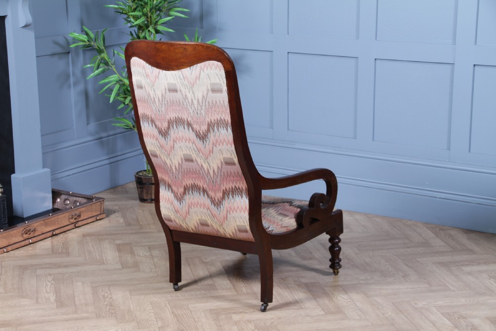 A high-backed Victorian mahogany fireside armchair featuring geometric flame-patterned upholstery, curved scroll armrests, turned front legs on brass castors, and a dark polished finish. View IX