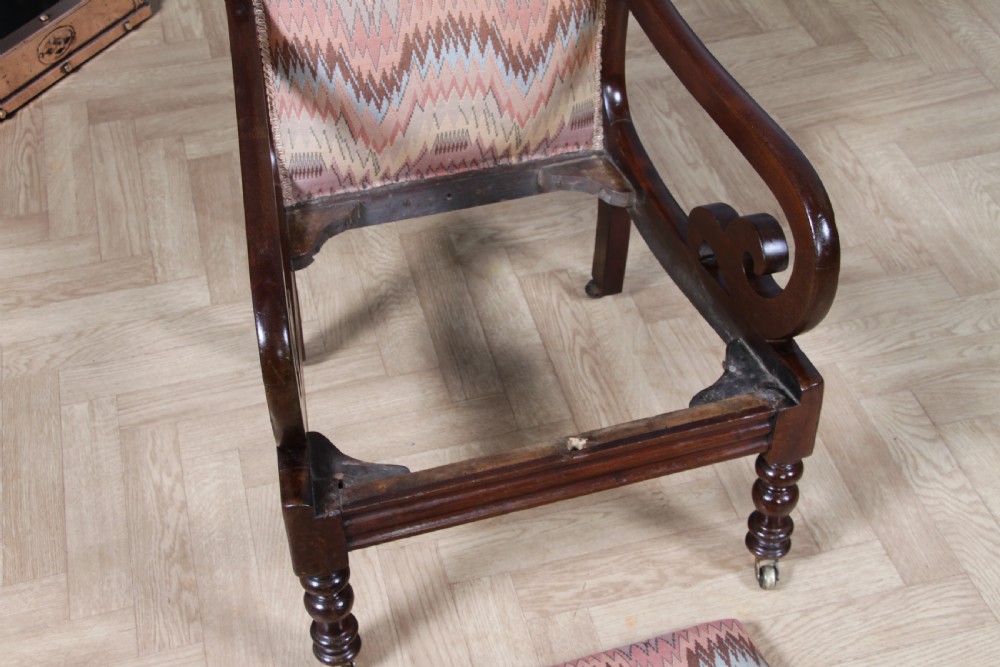A high-backed Victorian mahogany fireside armchair featuring geometric flame-patterned upholstery, curved scroll armrests, turned front legs on brass castors, and a dark polished finish. View XI
