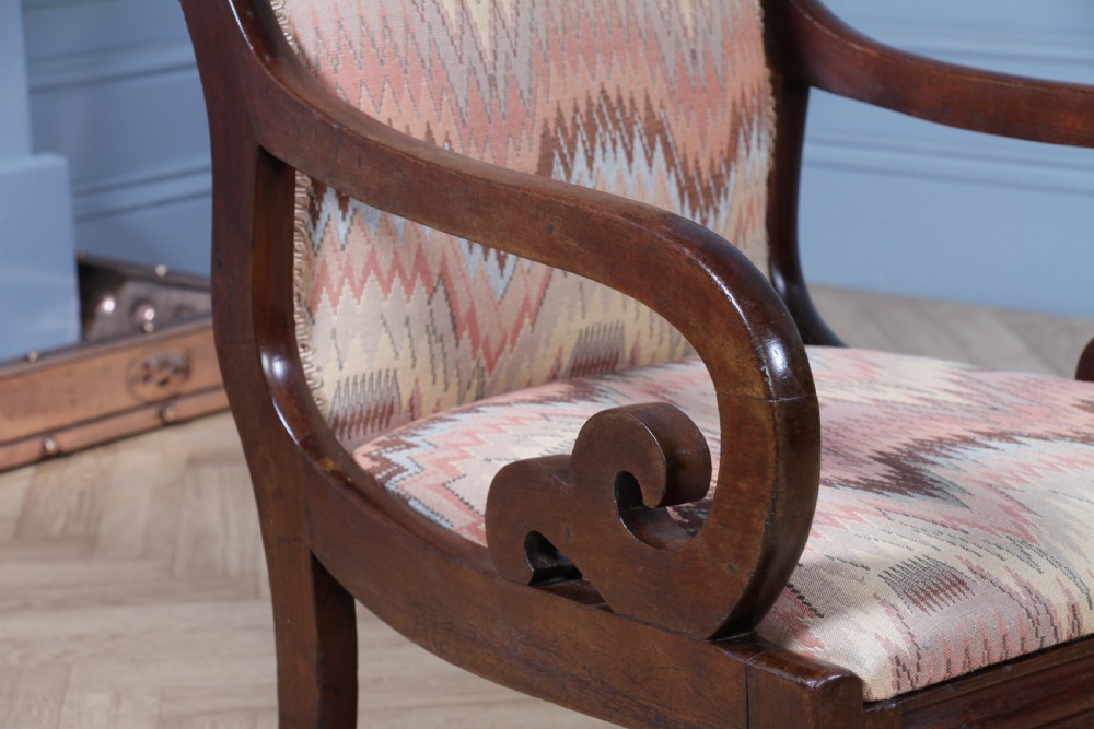 A high-backed Victorian mahogany fireside armchair featuring geometric flame-patterned upholstery, curved scroll armrests, turned front legs on brass castors, and a dark polished finish. View XIII