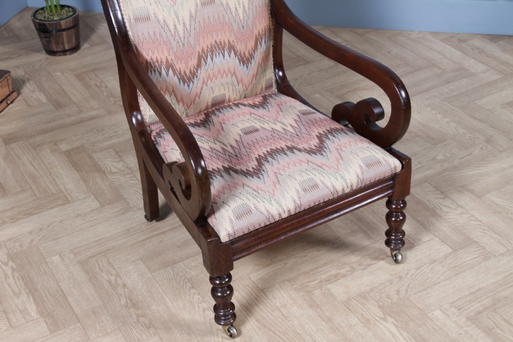A high-backed Victorian mahogany fireside armchair featuring geometric flame-patterned upholstery, curved scroll armrests, turned front legs on brass castors, and a dark polished finish. View XIV