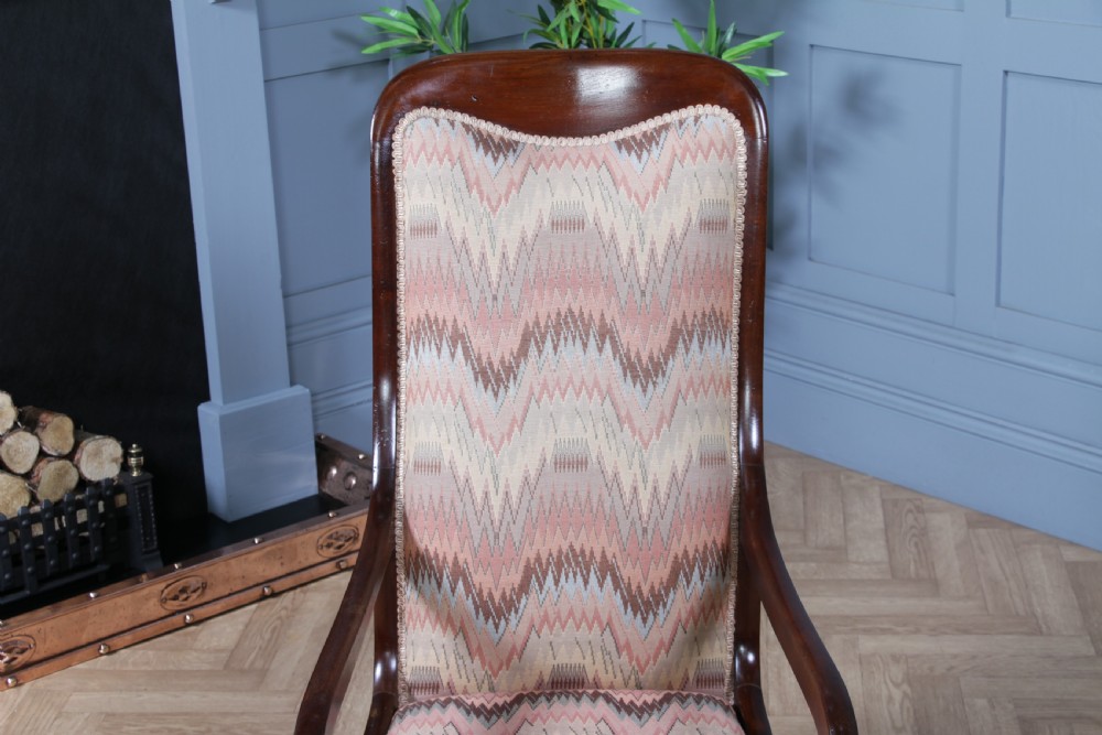 A high-backed Victorian mahogany fireside armchair featuring geometric flame-patterned upholstery, curved scroll armrests, turned front legs on brass castors, and a dark polished finish. View XVI