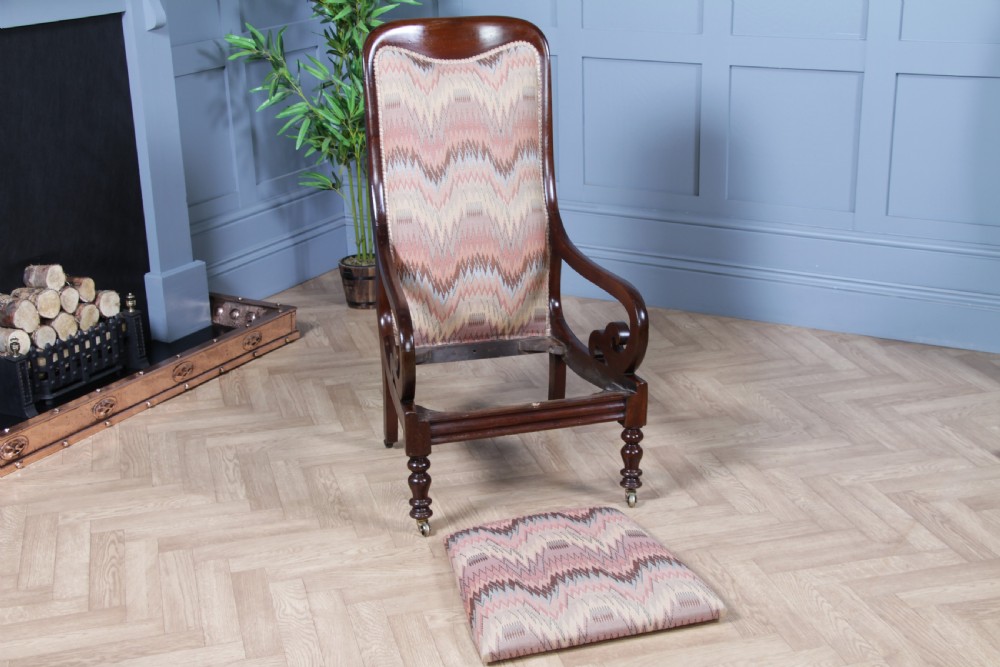 A high-backed Victorian mahogany fireside armchair featuring geometric flame-patterned upholstery, curved scroll armrests, turned front legs on brass castors, and a dark polished finish. View XVII