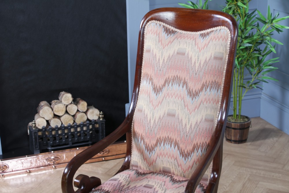 A high-backed Victorian mahogany fireside armchair featuring geometric flame-patterned upholstery, curved scroll armrests, turned front legs on brass castors, and a dark polished finish. View XVIII