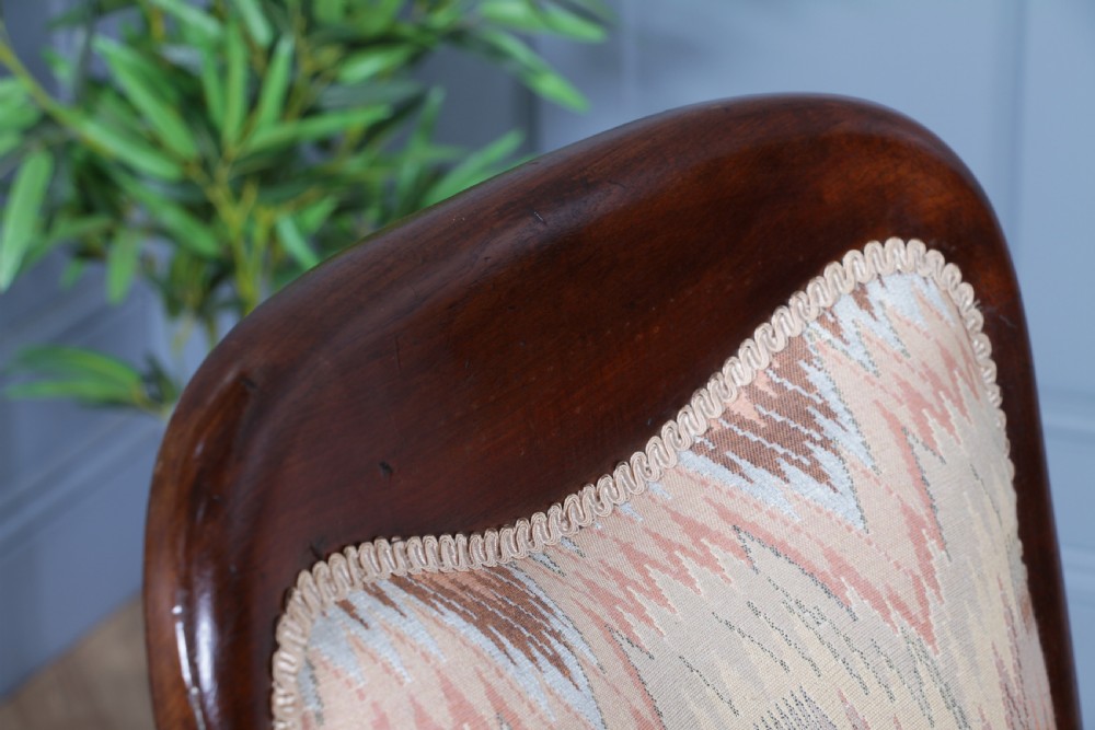 A high-backed Victorian mahogany fireside armchair featuring geometric flame-patterned upholstery, curved scroll armrests, turned front legs on brass castors, and a dark polished finish. View XIX