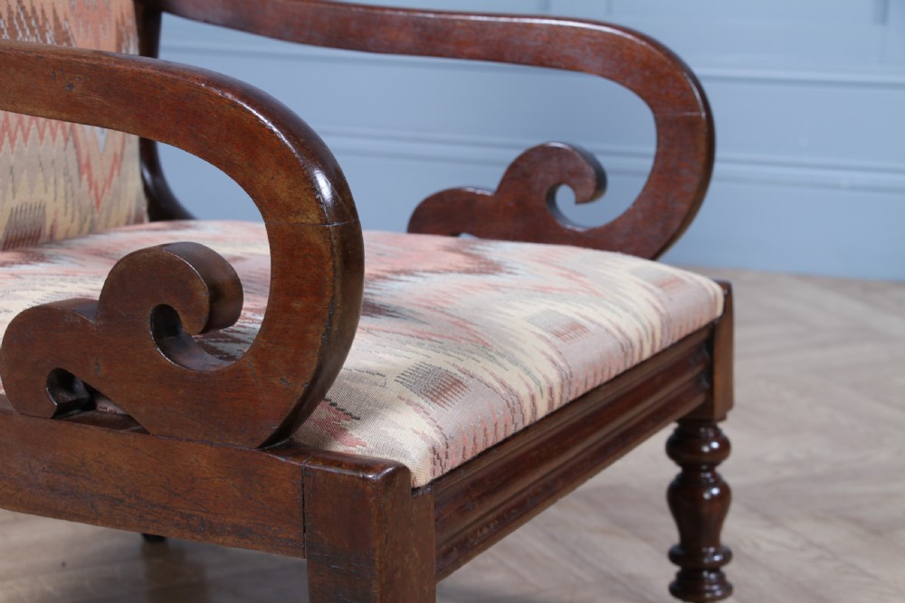 A high-backed Victorian mahogany fireside armchair featuring geometric flame-patterned upholstery, curved scroll armrests, turned front legs on brass castors, and a dark polished finish. View XX