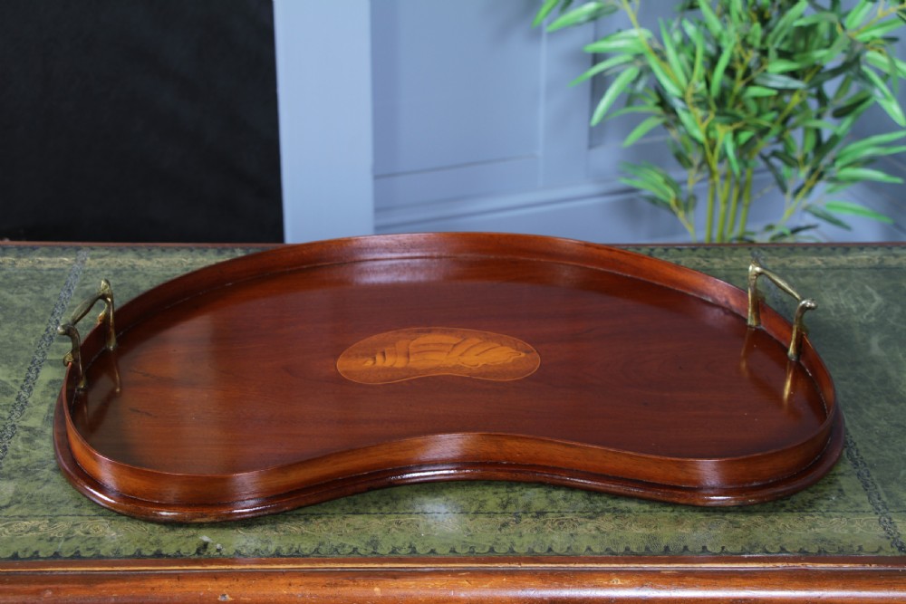 An Edwardian kidney-shaped solid mahogany serving tray featuring a central inlaid shell motif and two brass carrying handles. View V